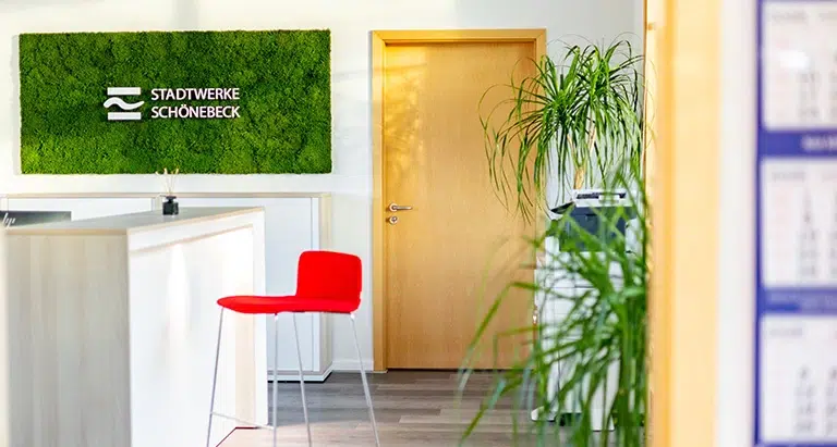 Grüne Mooswand mit Stadtwerke-Schönebeck-Logo über weißem Empfangstresen
